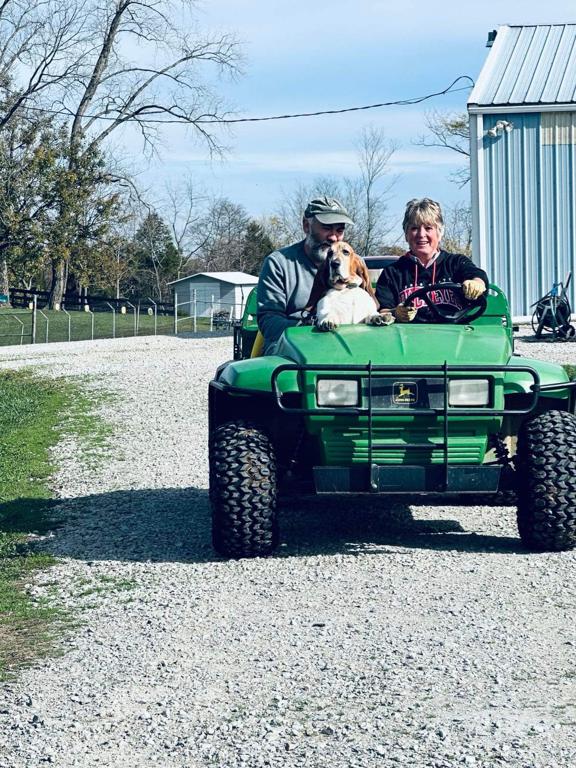A head on photo of two people on a Gater with a big chesty basset hound peering out the passenger's lap.