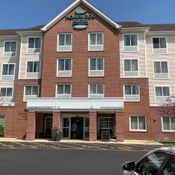 Front of four story Homewood Suites by Hilton hotel building. Red brick and tan vinyl siding facades.