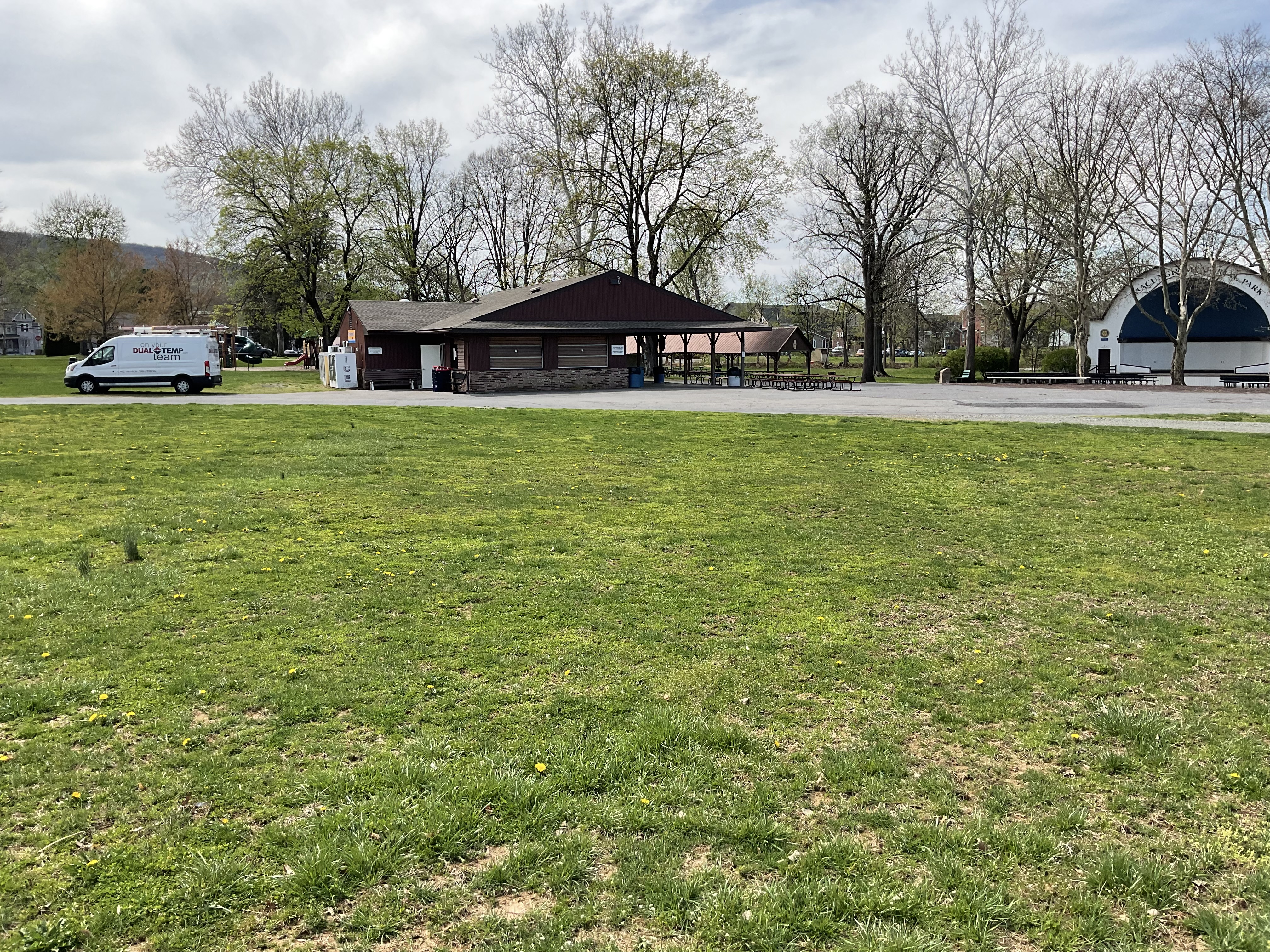 Grassy park with a building in the distance with a pavilion attached.