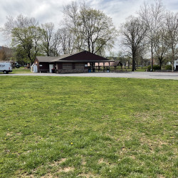Grassy park with a building in the distance with a pavilion attached.