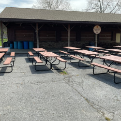 Building with an overhang with three rows of picnic tables in front of it.